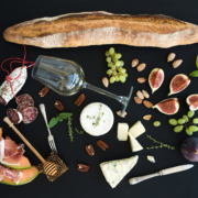 Wine and snack set. Baguette, glass of white, figs, grapes, nuts, cheese variety, meat appetizers, herbs on black grunge background, top view.